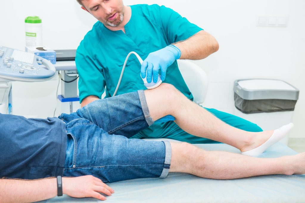 Orthopedist doctor conducting ultrasound examination of patient's knee in clinic