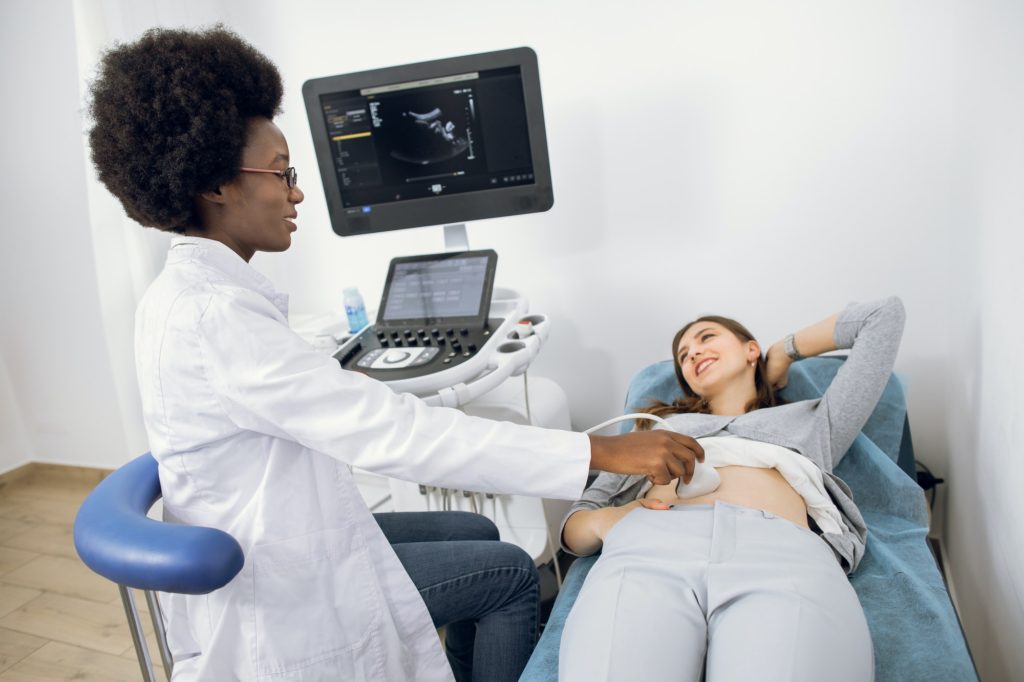 Young African female doctor using ultrasound machine in clinic, makes abdominal ultrasound for young